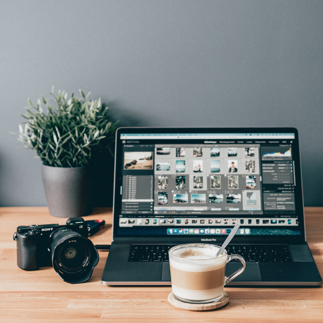 Laptop with digital photos on the screen and a camera and a cup of coffee nearby. 
